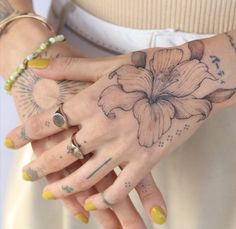 a woman's hands with tattoos and rings on her left hand, holding a yellow manicure