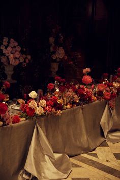 a long table covered with flowers and candles in front of a wall full of vases