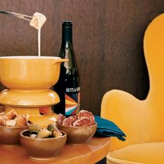 a table topped with bowls filled with food next to a bottle of wine and a yellow chair