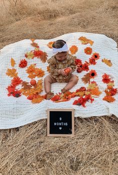 a baby sitting on a blanket with autumn leaves around it and a sign that says moms