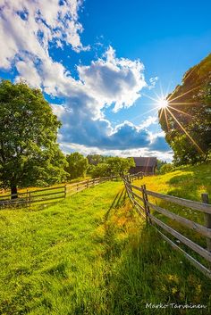 the sun shines brightly through the clouds over a field with a fence and trees