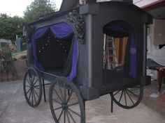 a horse drawn carriage with purple curtains on it's sides and black wheels, parked in front of a house