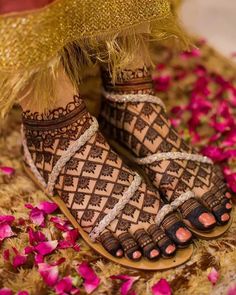 the feet and ankles of a woman with henna tattoos on their feet, standing in front of pink flowers