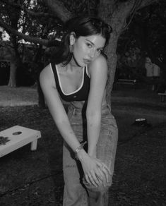 black and white photograph of a woman leaning against a tree with her hands on her hips