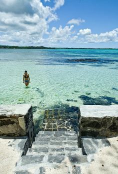 a woman standing in the water near steps leading to an ocean with blue sky and clouds