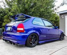 a blue car parked in front of a garage with its trunk open and the hood up