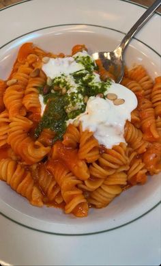 a white plate topped with pasta covered in sauce and toppings next to a fork