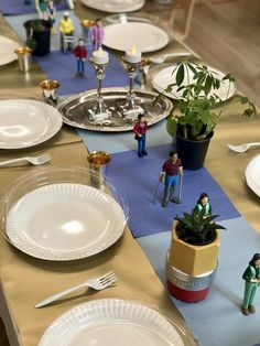 the table is set with white plates, silverware and small figurines on it