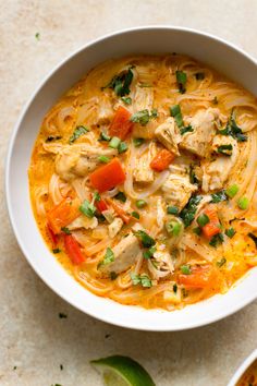 a white bowl filled with chicken noodle soup and garnished with cilantro