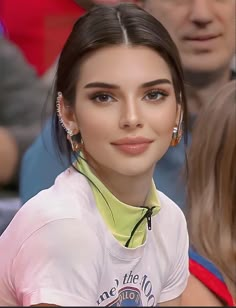 a close up of a person wearing earring's and a crowd behind her