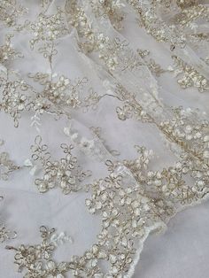 A beautiful ivory and gold tulle, it truly is a stunning tulle. It has Ivory thread embroidered flowers, outlined by a gold thread, and embellished with ivory coloured pearls. It has a double edged border.  The tulle is soft and has a good drape to it, making it ideal for any item of clothing, especially dresses, bridal or bridesmaid.  Width: 44 inch wide Sold of the roll, if you buy more than one meter, fabric will be in a continuous length. Although we have taken great care to portray the true Pearl Fabric, Gold Tulle, Pearl Lace, Dress Tutu, Gold Bridesmaid Dresses, Wedding Lace, Pearl And Lace, Embroidered Tulle, Gold Thread