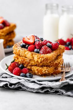 a stack of french toast with strawberries and blueberries on top, next to a glass of milk