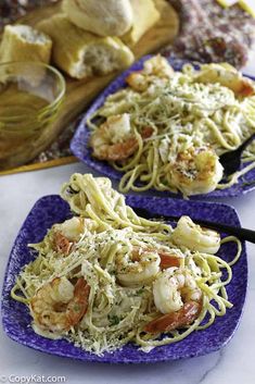 two plates filled with pasta and shrimp on top of a table next to garlic bread