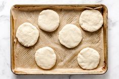 six uncooked pizza doughs on a baking sheet