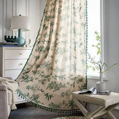 a living room with a chair, table and curtain in front of a window that has flowers on it