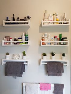 two white shelves with towels hanging on them and some plants in the middle one shelf is filled with personal care items