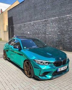 a blue car parked in front of a brick wall with black rims on it