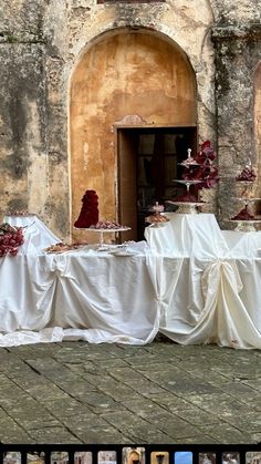 the table is covered with white cloths and red cake stands are in front of an old building