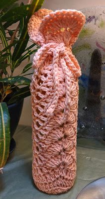 a crocheted vase sitting on top of a table next to a potted plant