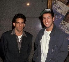 two men standing next to each other in front of a wall with posters on it