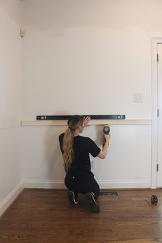 a woman is sitting on the floor working on a wall mounted shelf with two screwdrivers