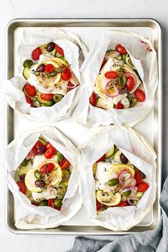 four pita breads with tomatoes, olives and other toppings on a baking sheet