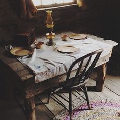 the table is set for two with plates and cups on it, near a window