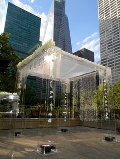 an artistic sculpture in the middle of a city square with skyscrapers behind it and people sitting on benches