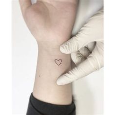 a person with a small heart tattoo on their left wrist and the other hand behind them