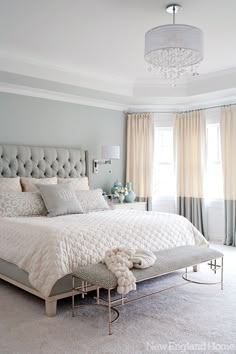 a bedroom with a large bed, chandelier and two windows in the background