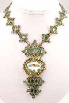 an elaborate necklace with green beads on a white mannequin