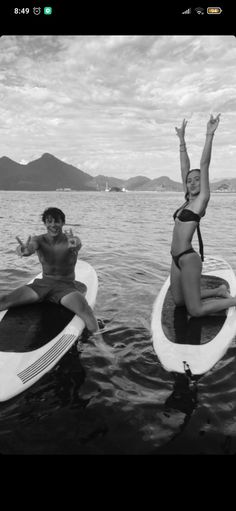 two women on surfboards in the water with their arms up and one holding her hand out