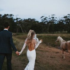 the bride and groom are holding hands as they walk with their horses through the field