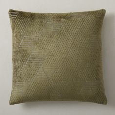 an olive green pillow with silver threading on the front and back, sitting against a white wall