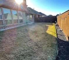 the sun shines brightly over a yard in front of a brick house and fence