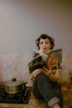 a woman sitting on the kitchen counter reading a magazine