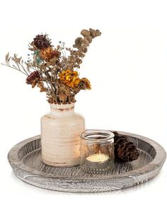 a white vase with flowers in it sitting on a tray next to a lit candle