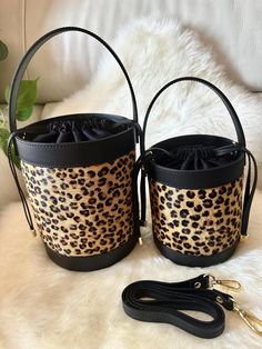 two leopard print buckets with black straps on a white fur rug next to a leash