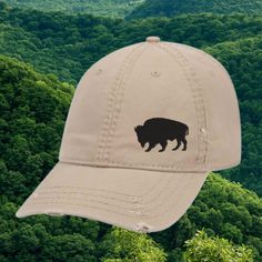 100% cotton twill, soft and unstructured 6 panel low-fitting dad hat. One size fit most adults. Elevate your everyday style with this vintage khaki baseball cap, featuring an embroidered silhouette of a majestic buffalo. Perfect for outdoor enthusiasts, this distressed dad hat adds a rugged touch to any outfit. The adjustable strap ensures a comfortable fit for both men and women, making it a versatile accessory for anyone who loves the wild and untamed spirit of the American West. Whether you'r Buffalo Hat, Embroidered Silhouette, Ranch Wyoming, Buffalo Ranch, Western Apparel, Distressed Hat, Color Complement, American West, Khaki Color