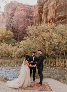 a bride and groom exchanging vows in front of a river with cliffs in the background