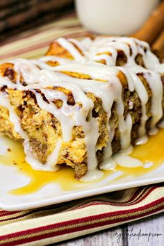 cinnamon roll with icing on a plate next to cinnamon sticks and a glass of milk