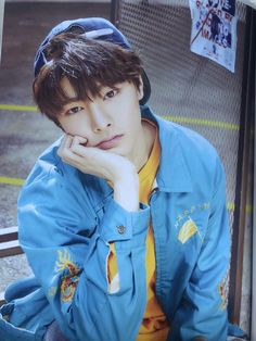 a young man sitting on top of a bench wearing a blue jacket and yellow shirt