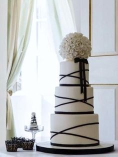 a white and black wedding cake sitting on top of a table next to a window