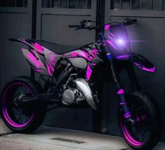 a pink and black motorcycle parked in front of a garage door with its lights on