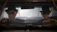 two men sitting in the back of a car with hats and sunglasses on their heads