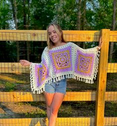 a woman standing in front of a fence with a crocheted shawl on her shoulders