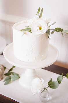 there is a white cake with flowers on the top of it and greenery around it