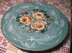 a plate with flowers painted on it sitting on a checkered tablecloth covered table