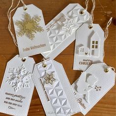 four tags are hanging from strings on a wooden table with white paper and gold foil