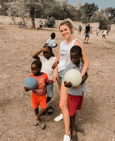 a woman and three children holding balls in the dirt